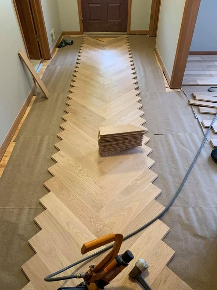 Hallway with herringbone wood flooring under installation, tools and materials visible on the floor.
