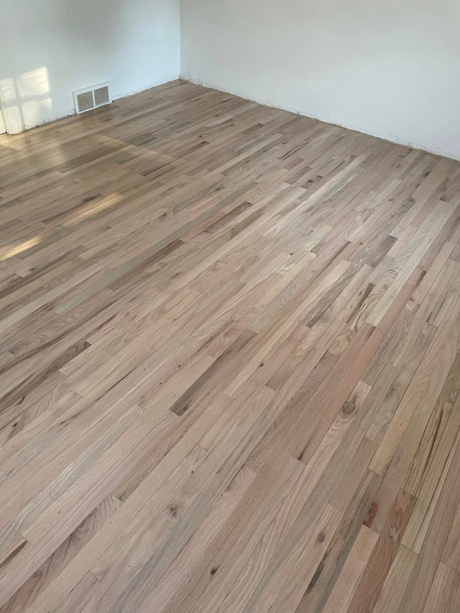 Empty room with light wood flooring and white walls, corner view.