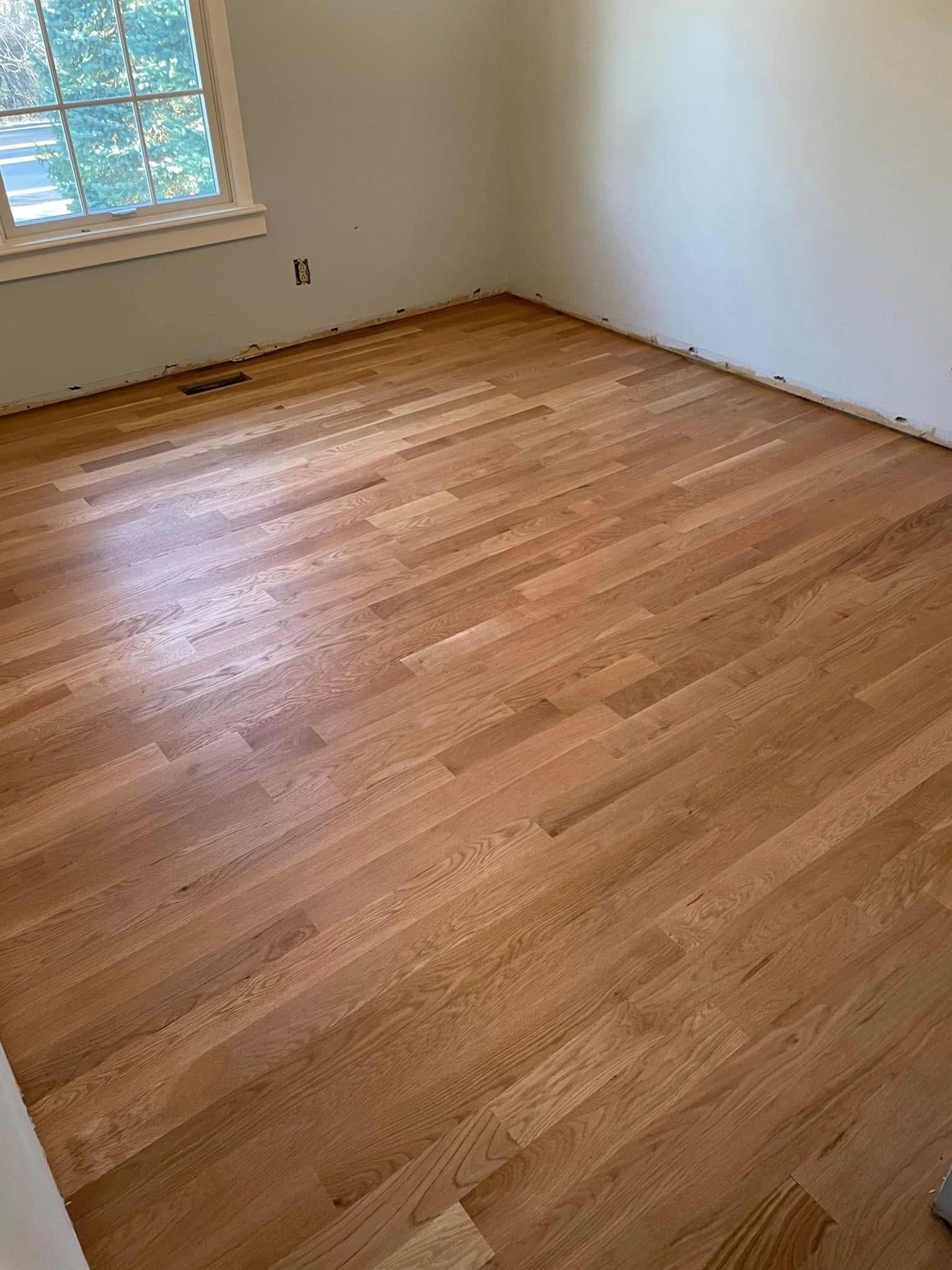 Empty room with light wood floors, white walls, and a window on the left.