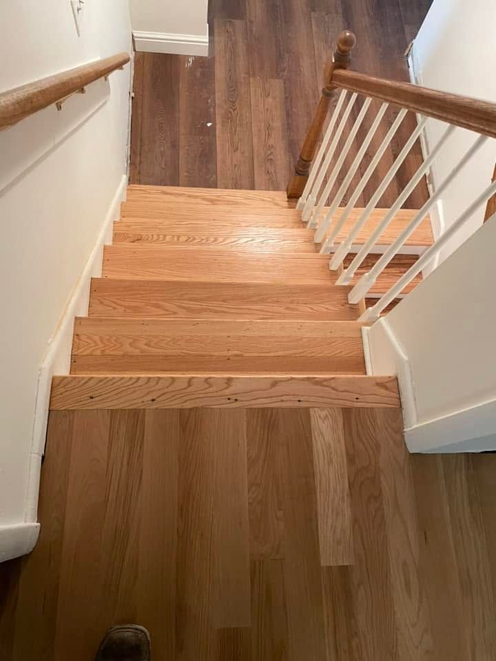 Wooden staircase with white railings and brown carpeted landing, viewed from the top.