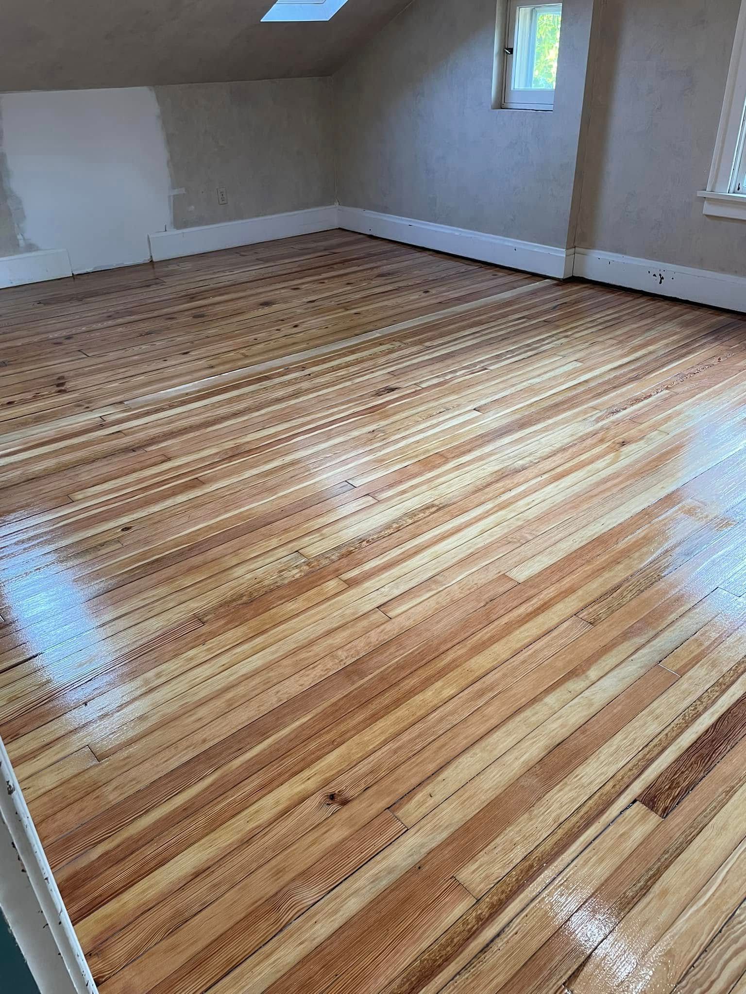 Empty room with freshly sanded wooden floor, white walls, and a small window.