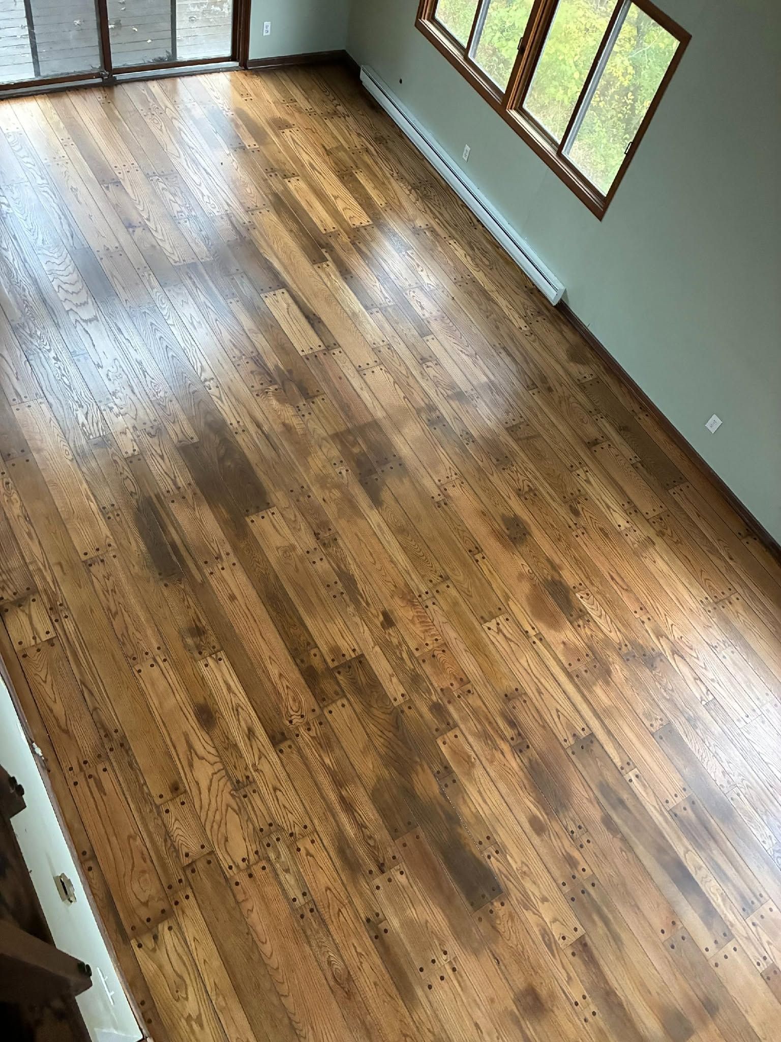 Empty room with polished hardwood floors, white walls, and large windows letting in natural light.