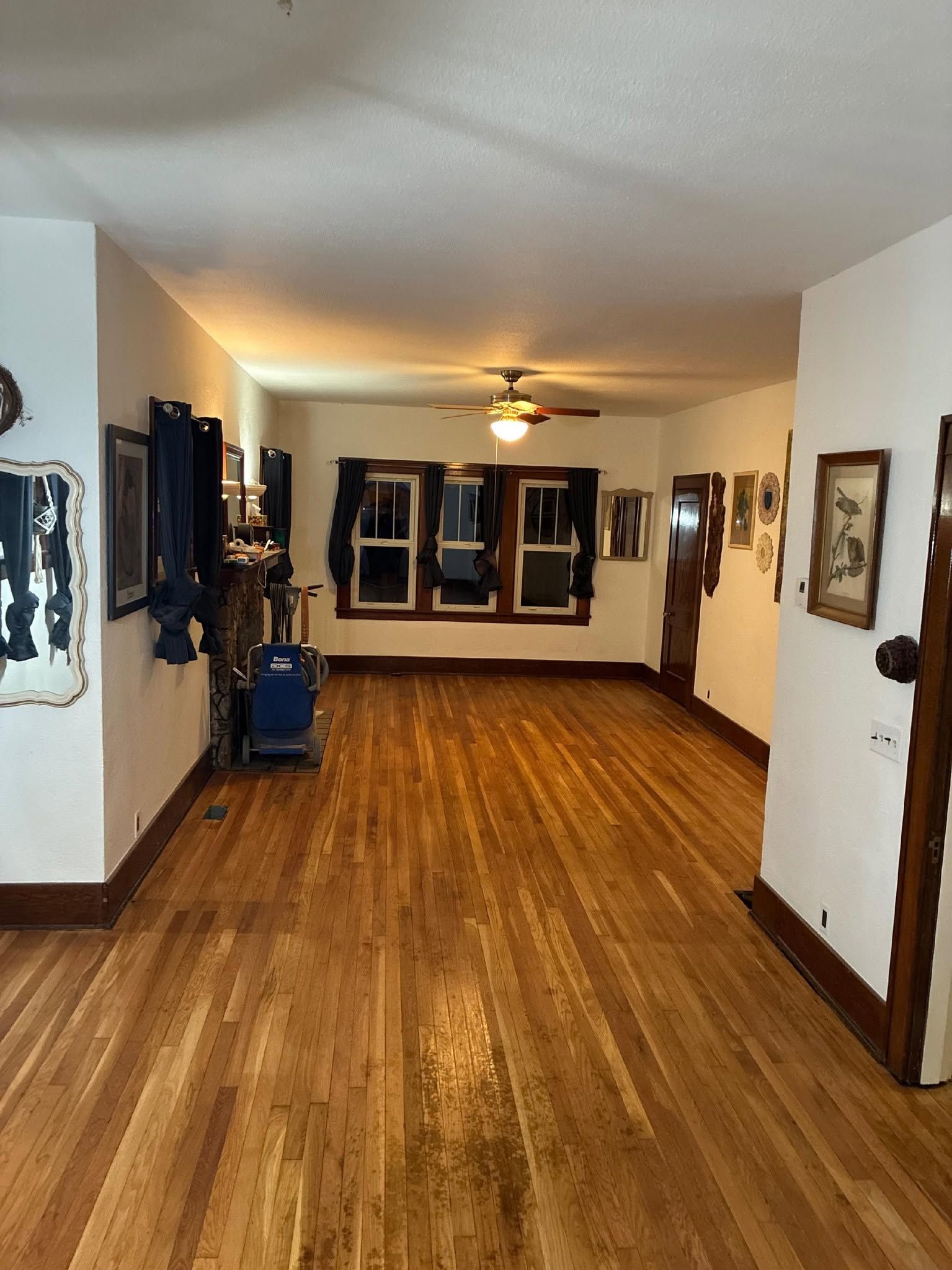 Long, narrow hallway with wood floors, white walls, framed art, and windows at the far end.