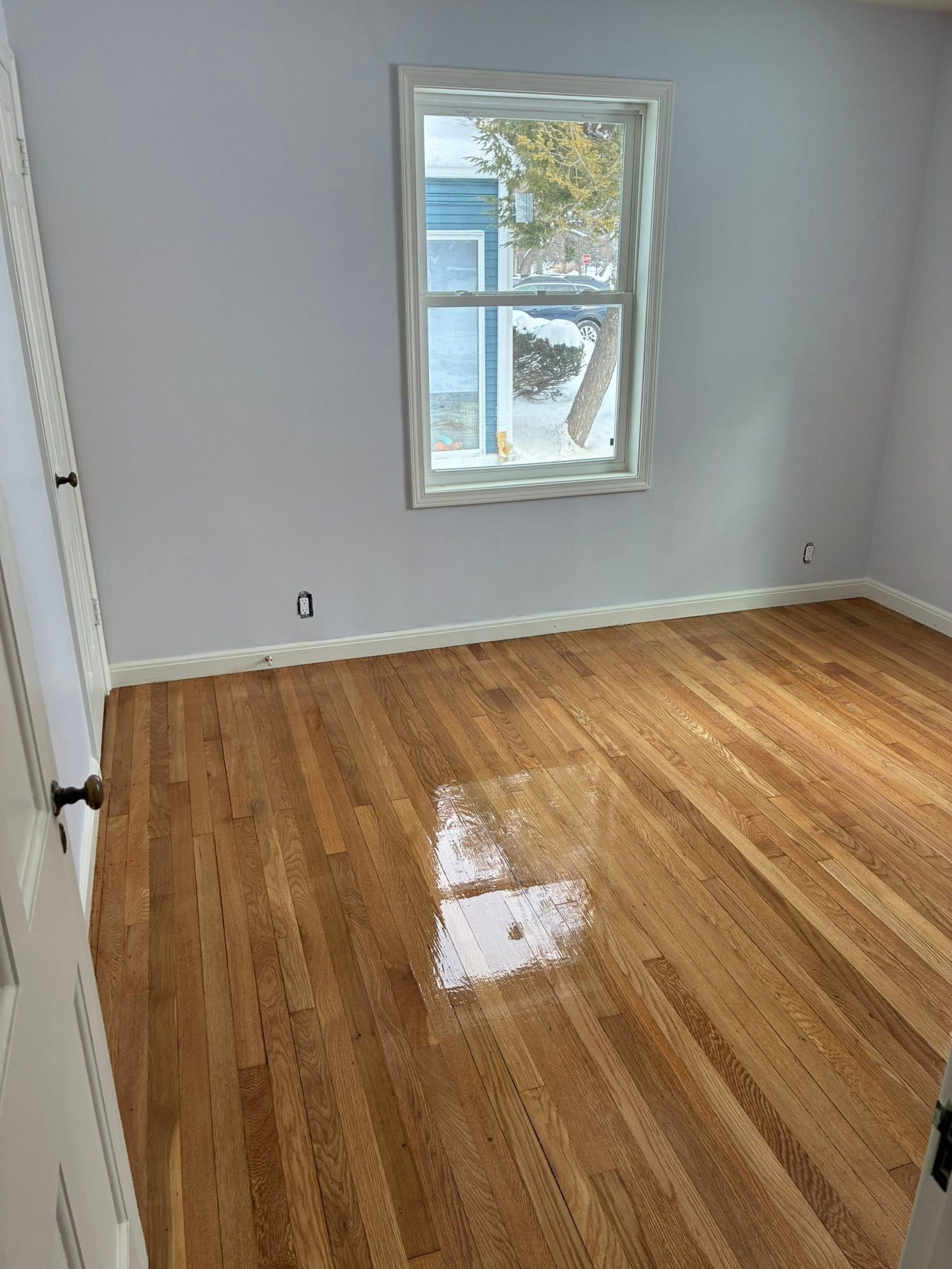 Empty room with hardwood floor and a single window on a light gray wall.