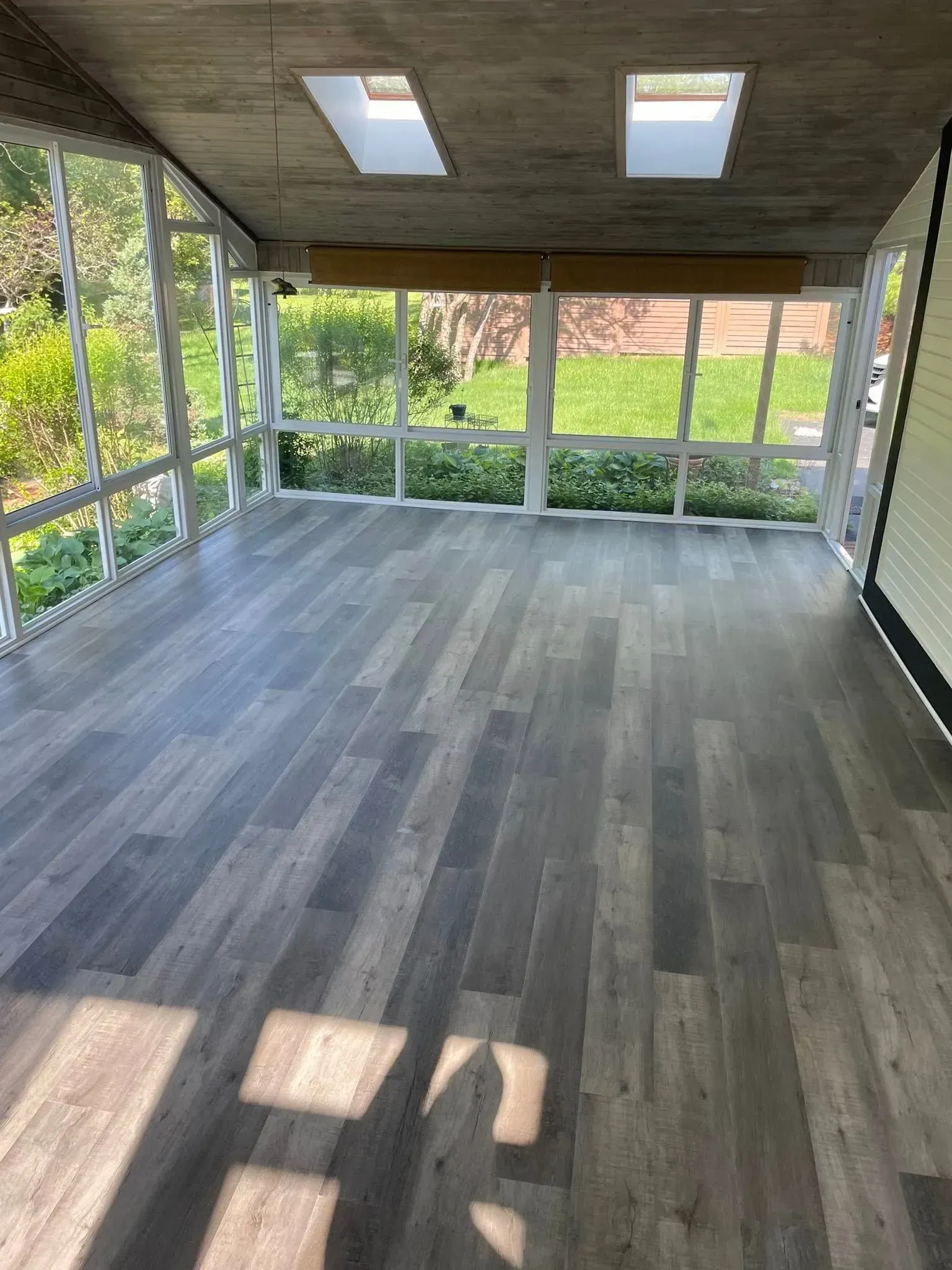 Sunroom with wood-look flooring, screened walls, and skylights overlooking greenery