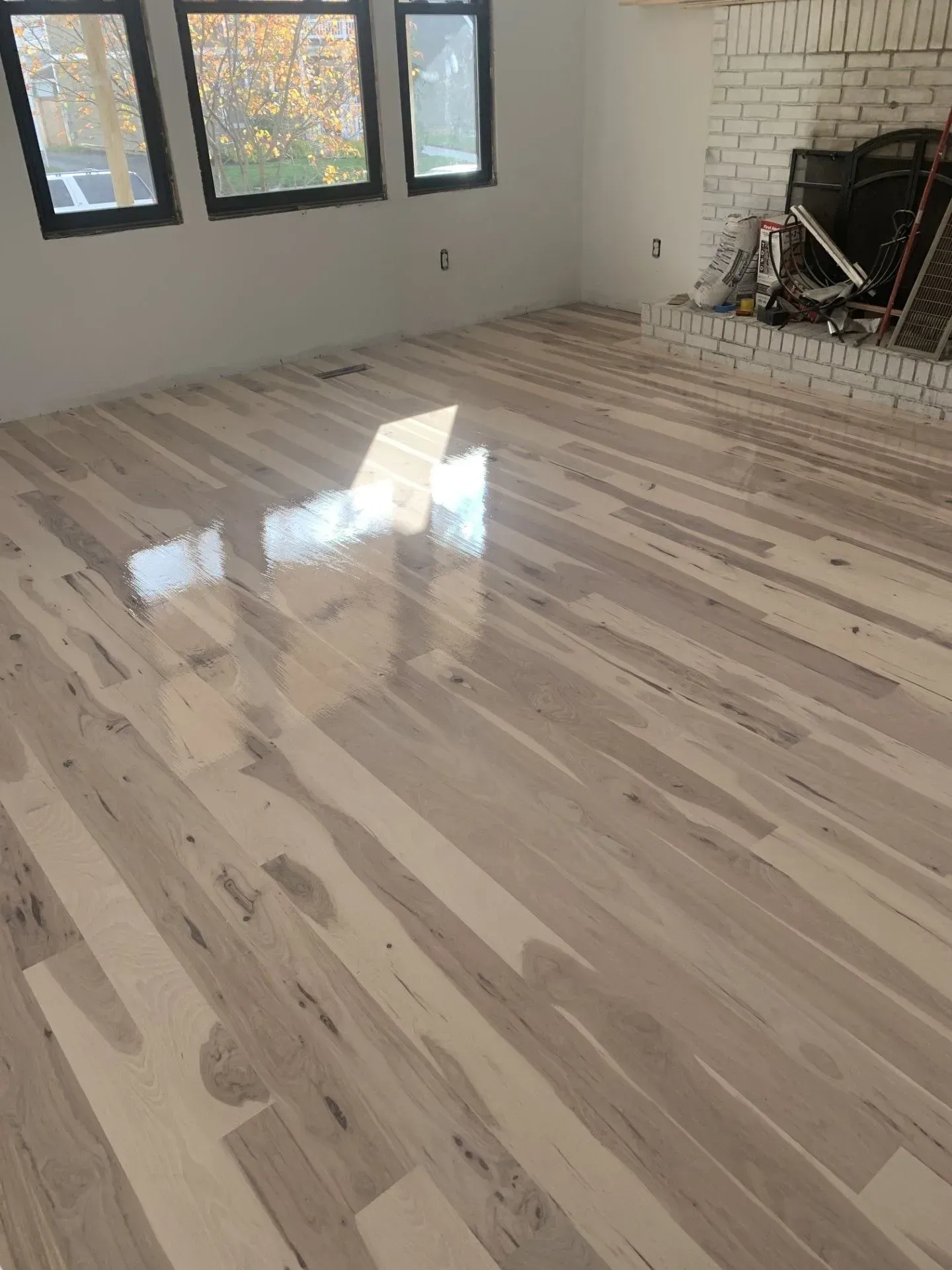 Empty room with light wood floors, windows, and a fireplace hearth, reflecting sunlight