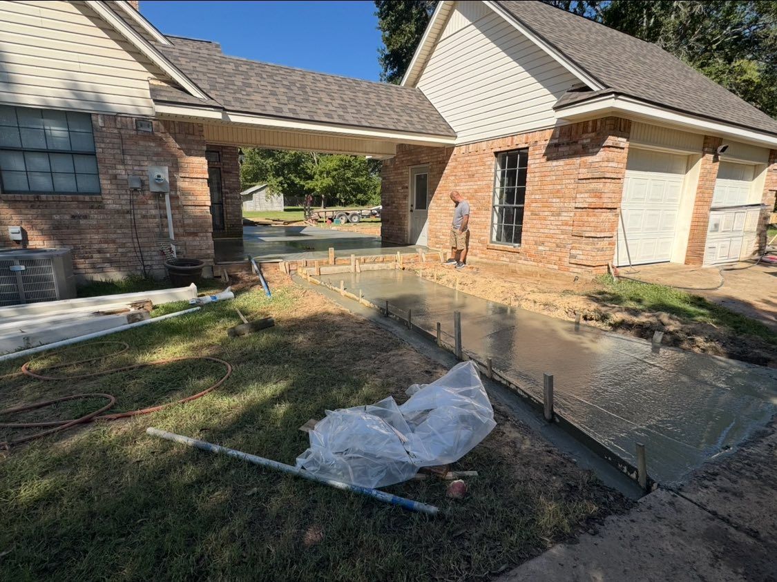 A newly poured concrete walkway leads to a house with a brick exterior and a carport.
