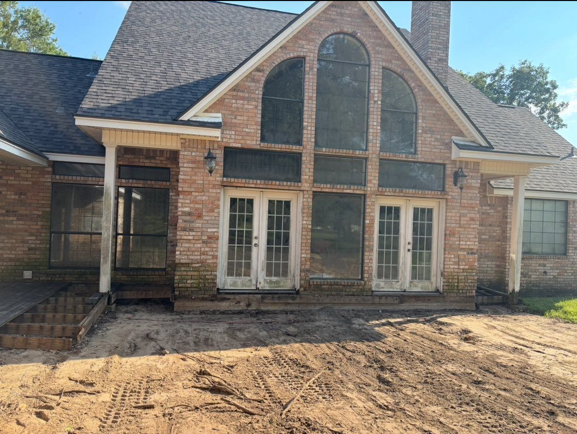 A large, two-story brick house with a prominent arched window and twin sets of glass doors, facing a patch of bare dirt.