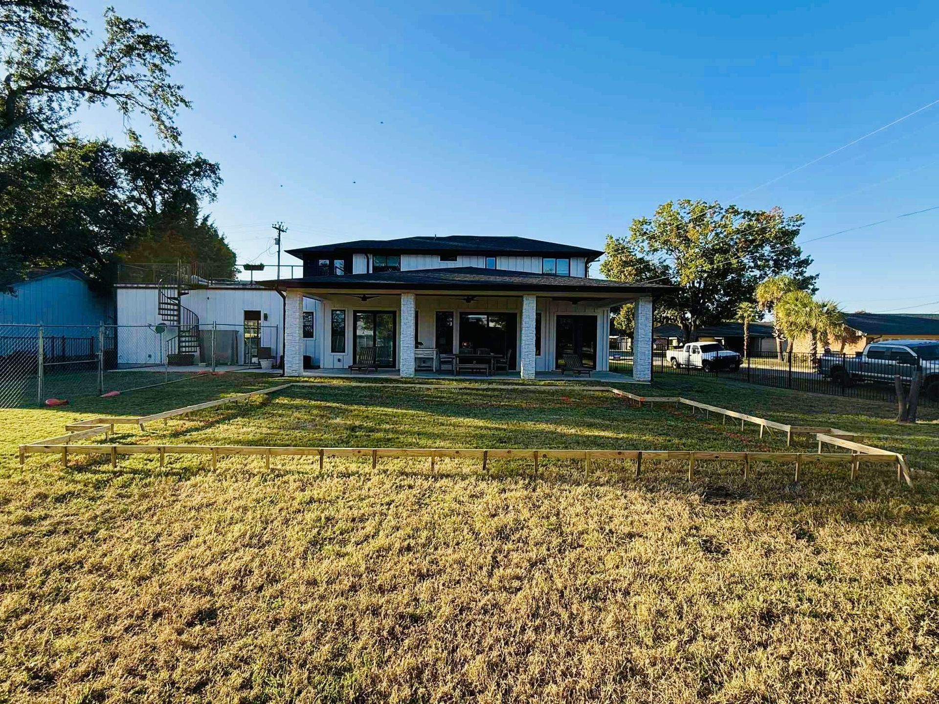 A white, two-story house with a covered patio, viewed from a yard with dried grass under a clear blue sky.