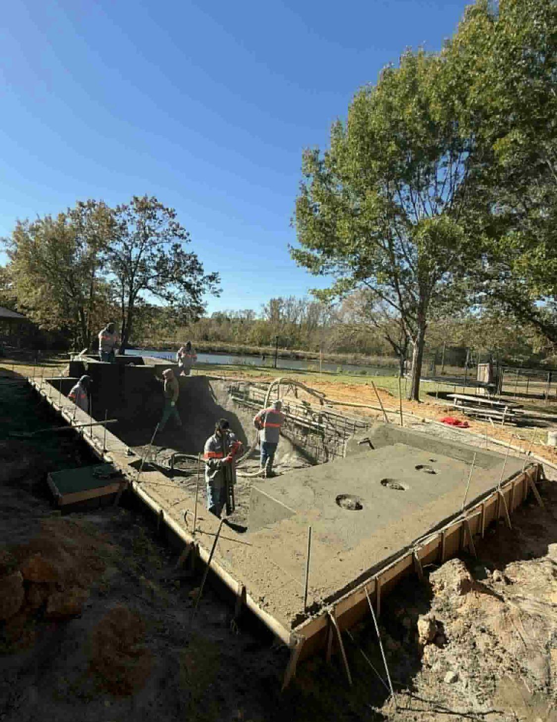 Workers pouring concrete into the rectangular frame of a backyard swimming pool under construction on a sunny day.