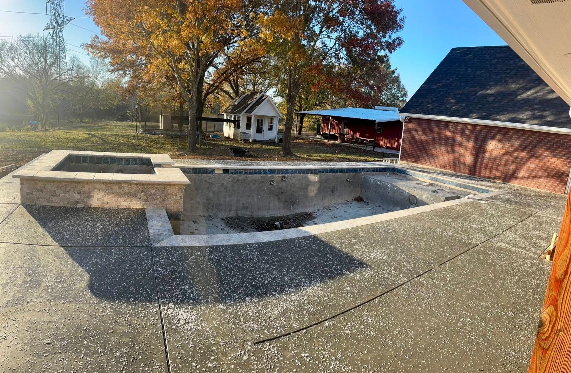An empty, rectangular swimming pool with an attached raised fire pit under construction on a concrete patio.
