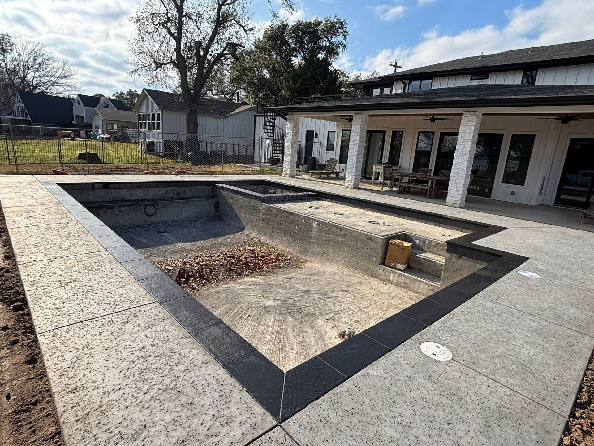 An empty, rectangular swimming pool under construction with gray concrete decking and a black stone border.