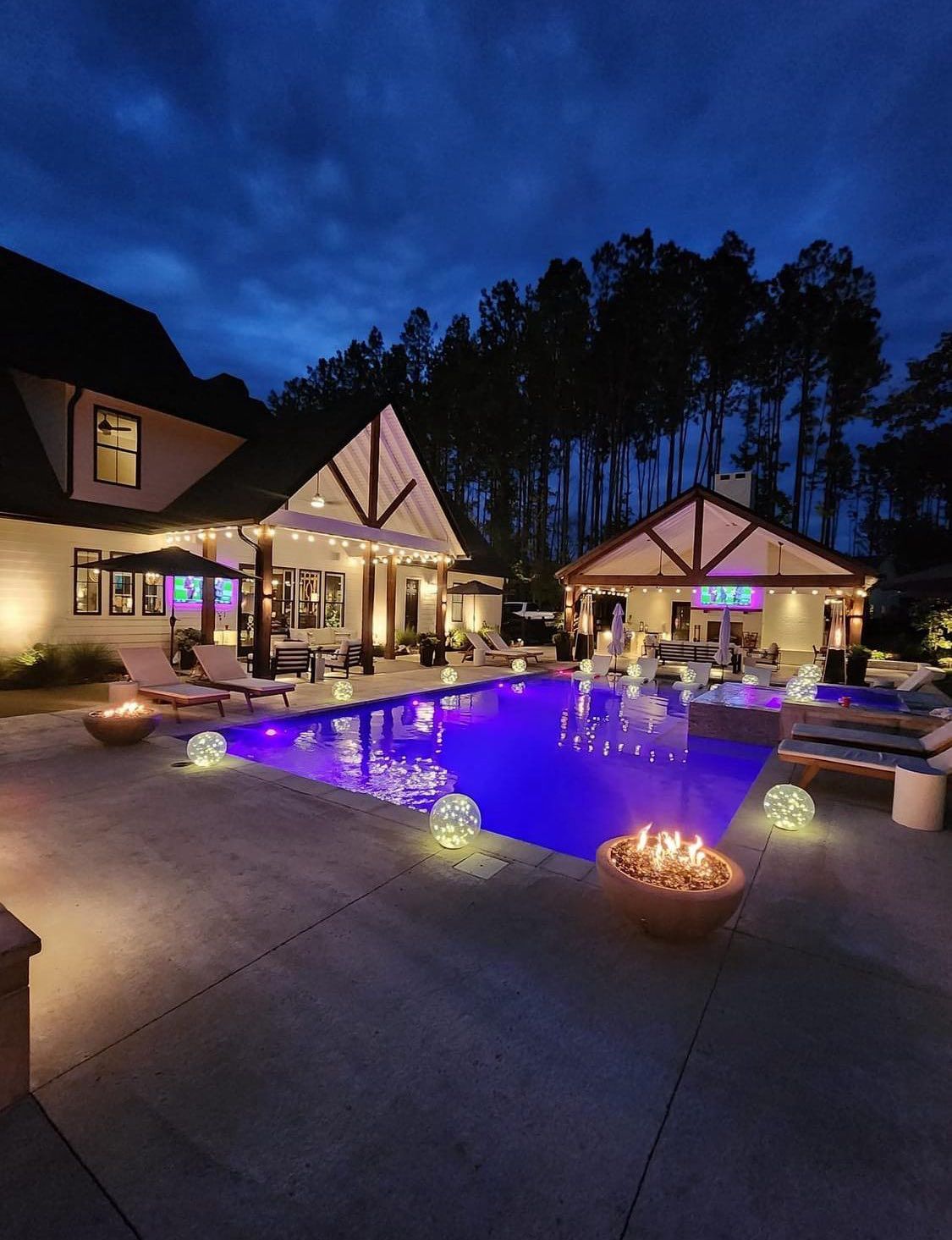 A backyard swimming pool at twilight with glowing sphere lights, lounge chairs, and an illuminated outdoor structure.