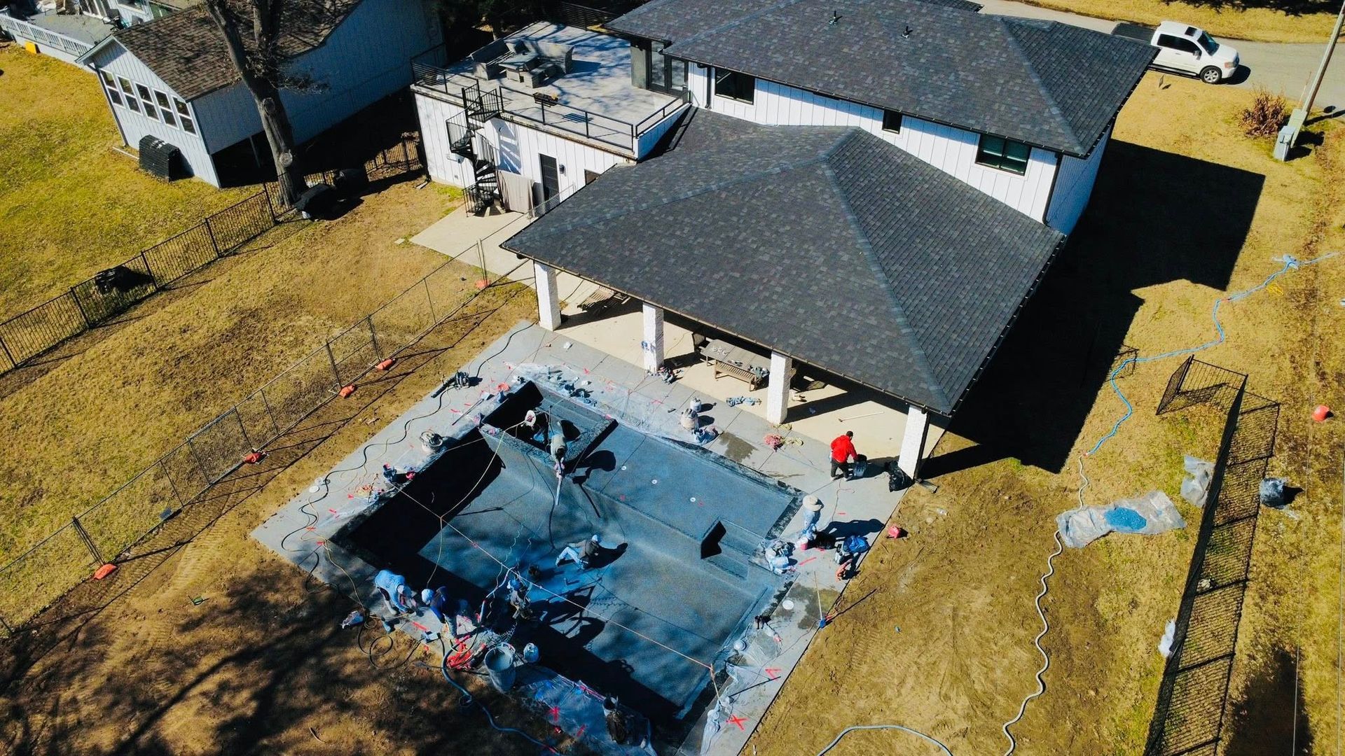 An aerial view of a house backyard with a partially covered swimming pool under construction and workers present.
