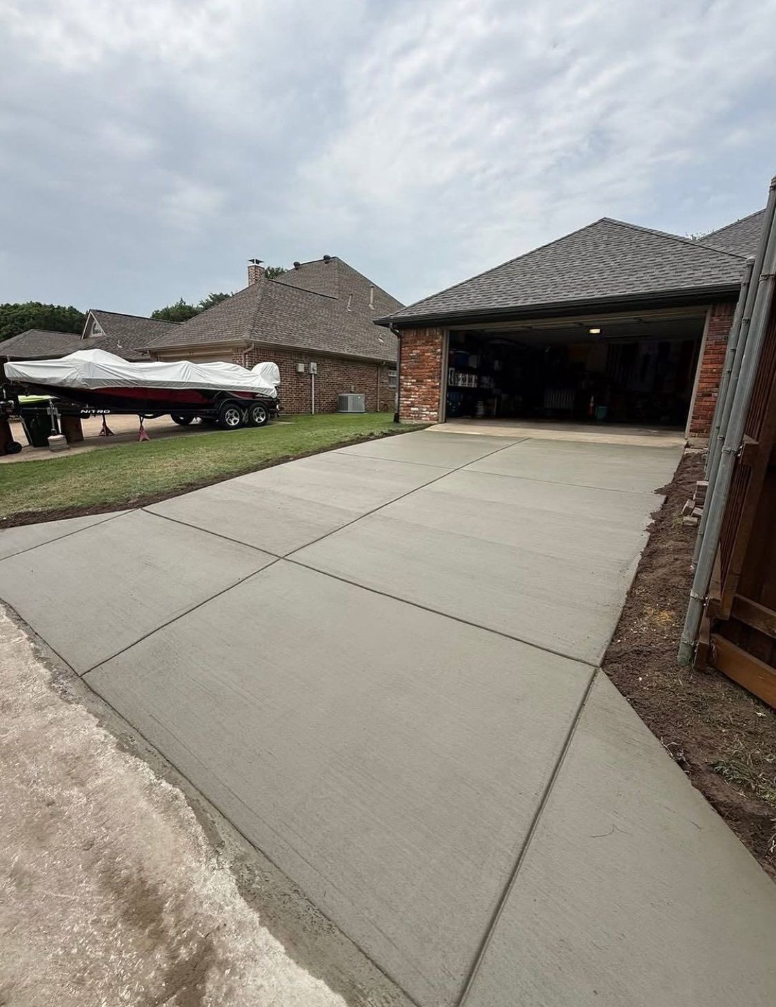 A freshly poured concrete driveway leading to a two-car garage, with a boat on a trailer parked on the adjacent lawn.