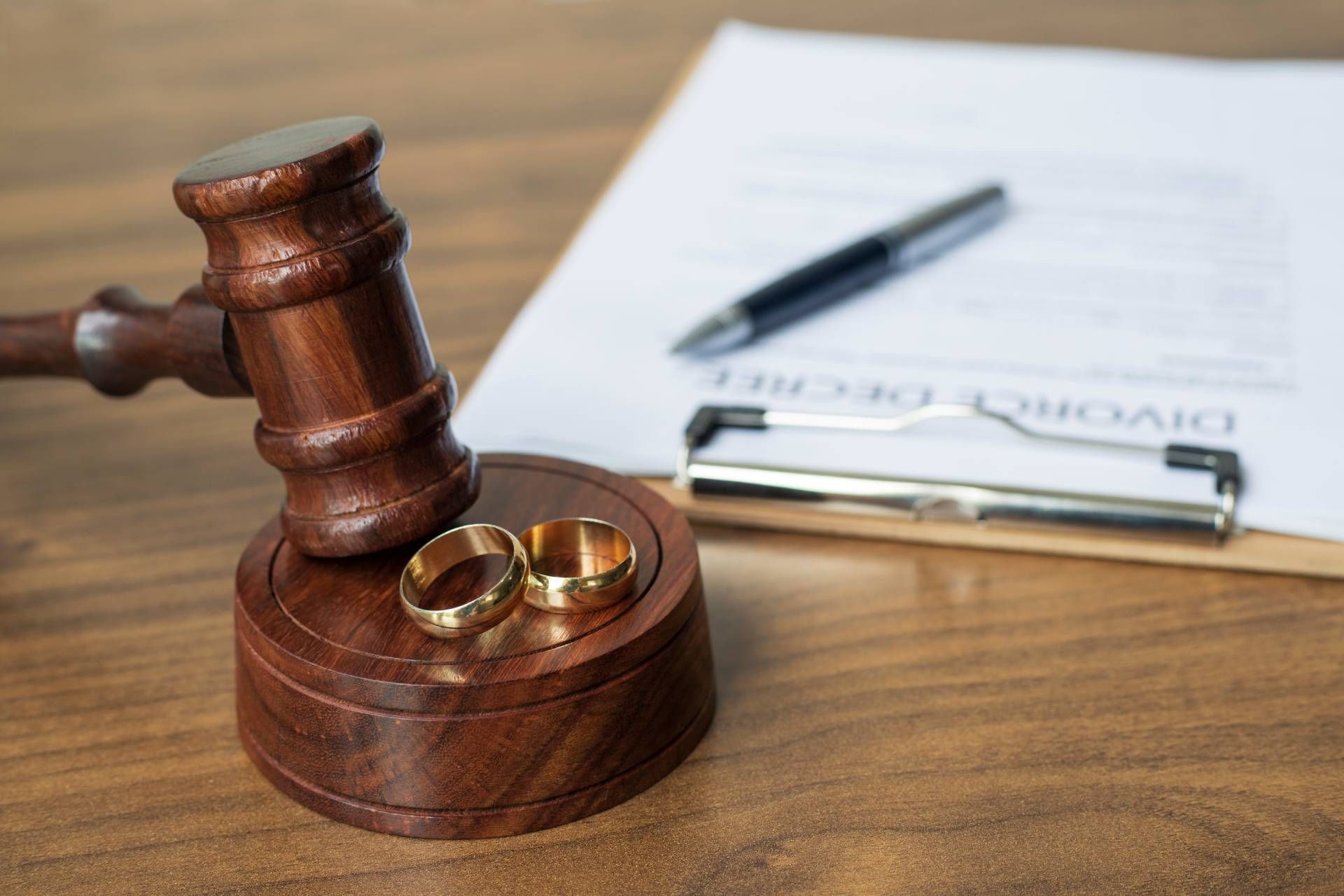Wedding rings on a wooden gavel beside signed paperwork and a pen.