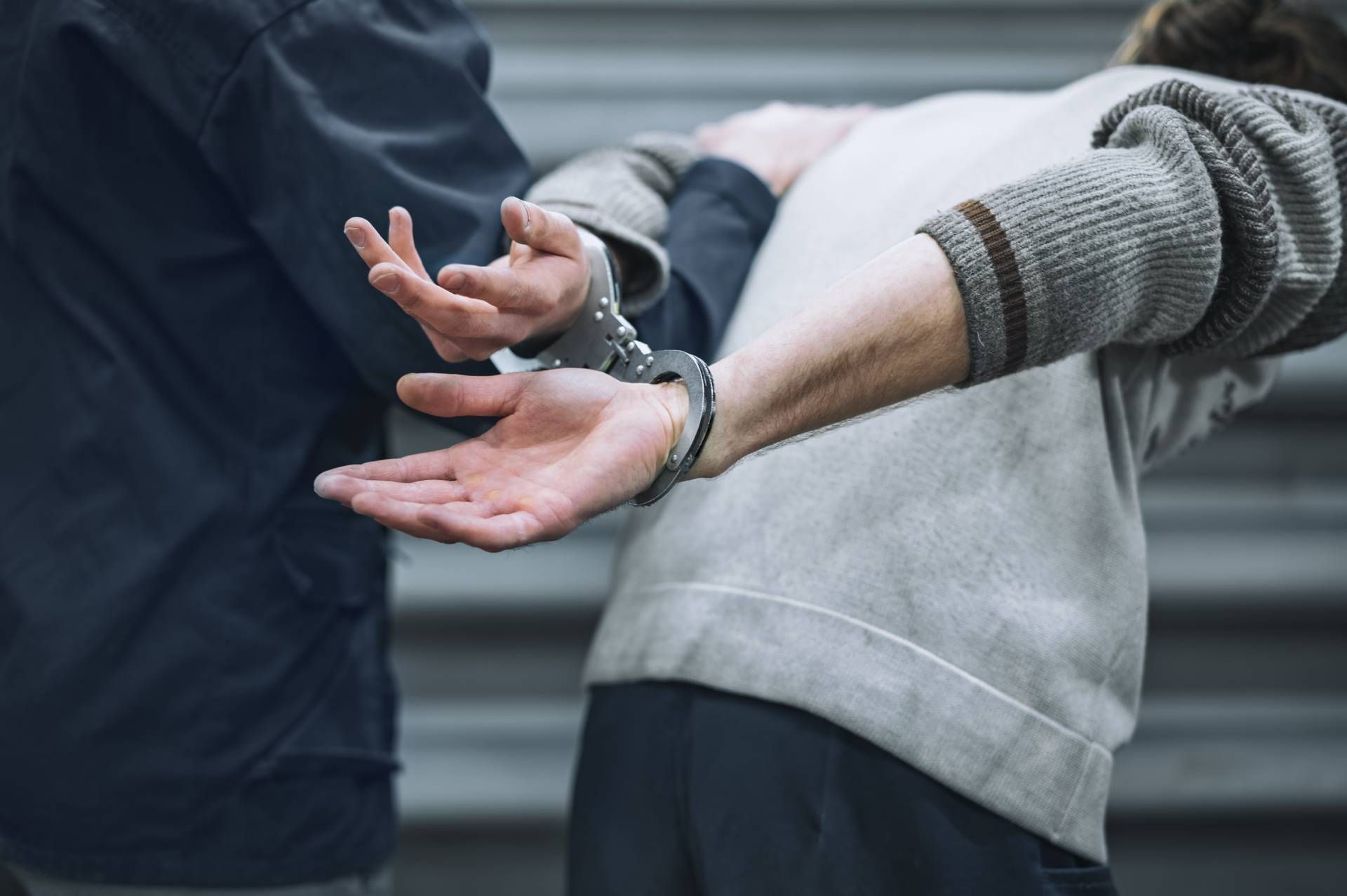 A police officer in uniform handcuffs a person standing next to an open patrol car door.