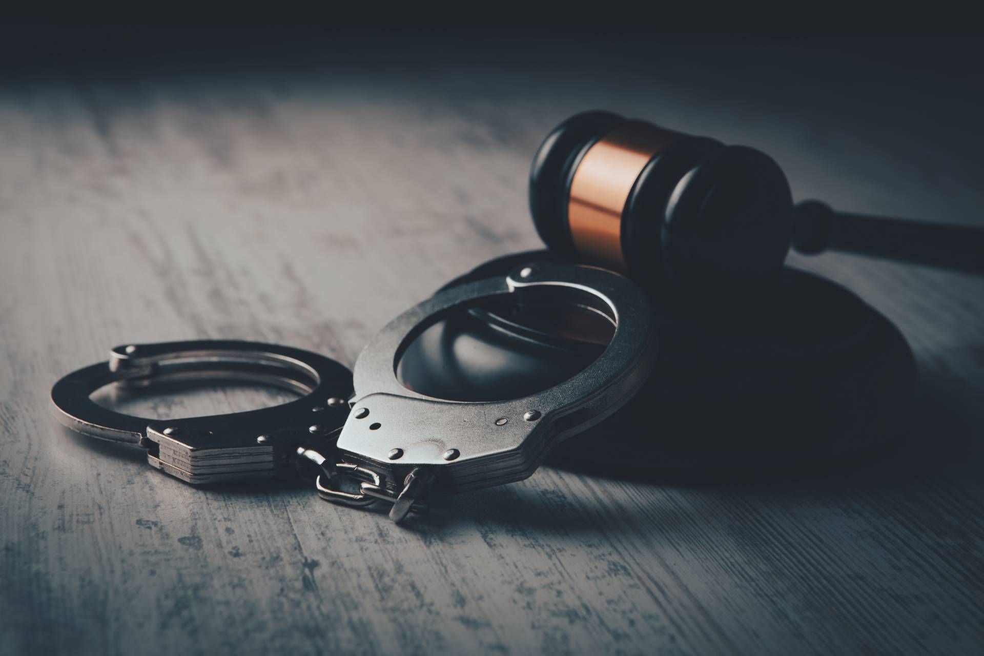 Handcuffs next to a gavel on a light-colored wooden surface, suggesting law and justice.