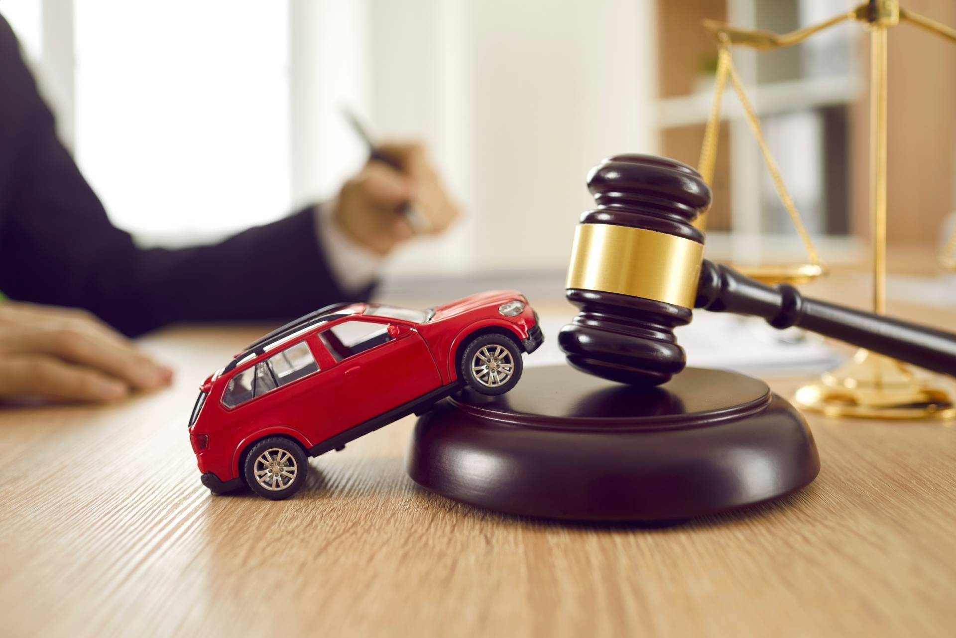 Toy car crashed near a gavel, scales of justice in background, lawyer at desk.
