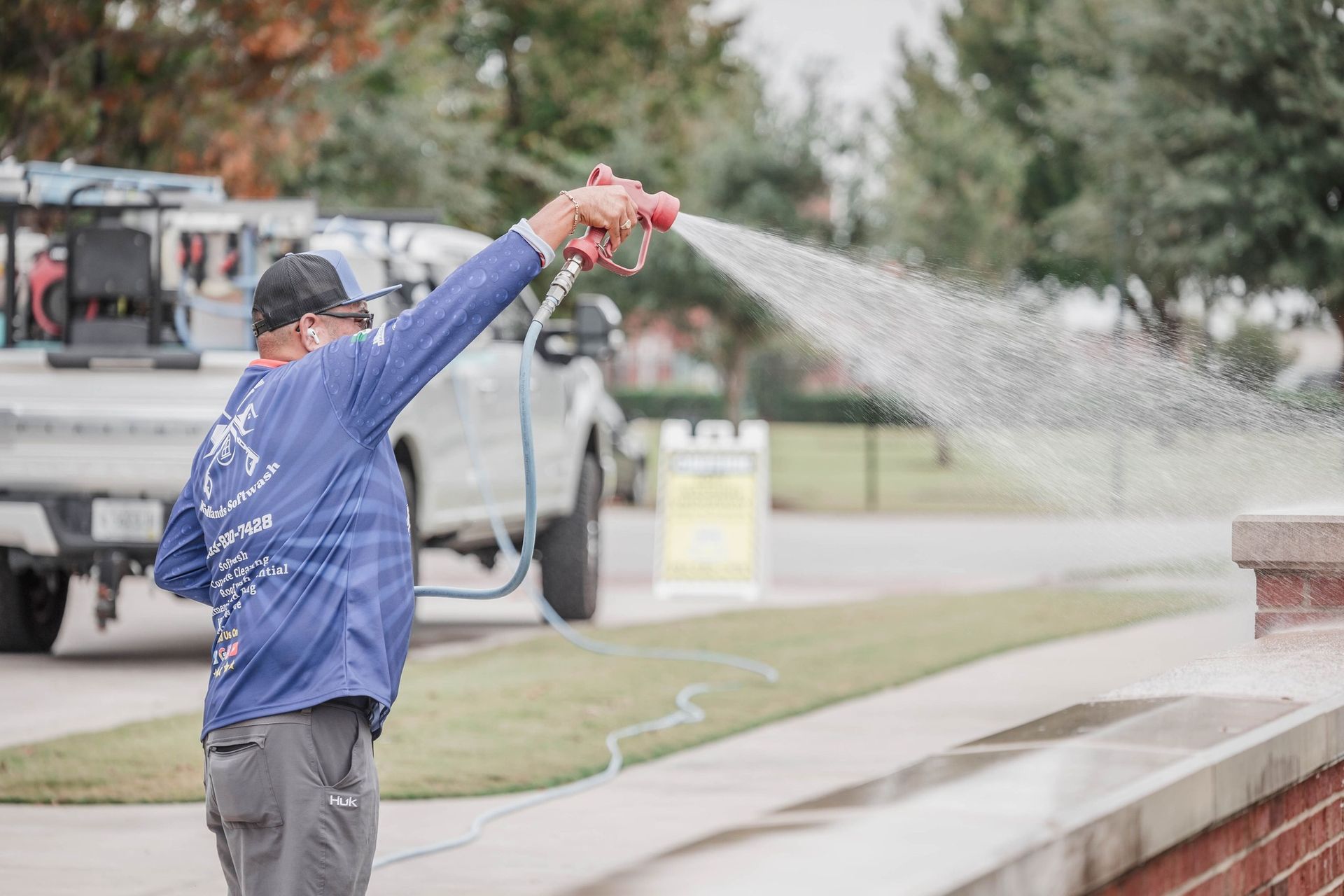 A man is spraying water on a brick wall with a hose.