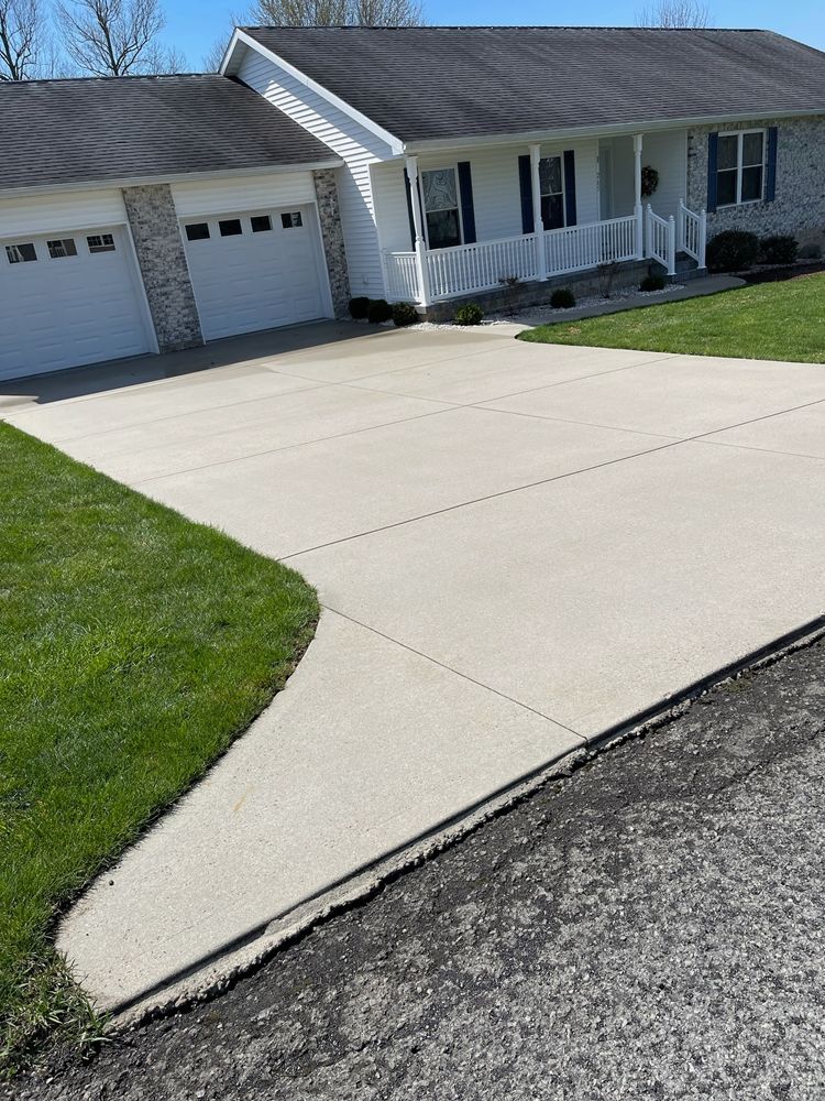 Concrete driveway leading to a white house with an attached garage and green lawn.