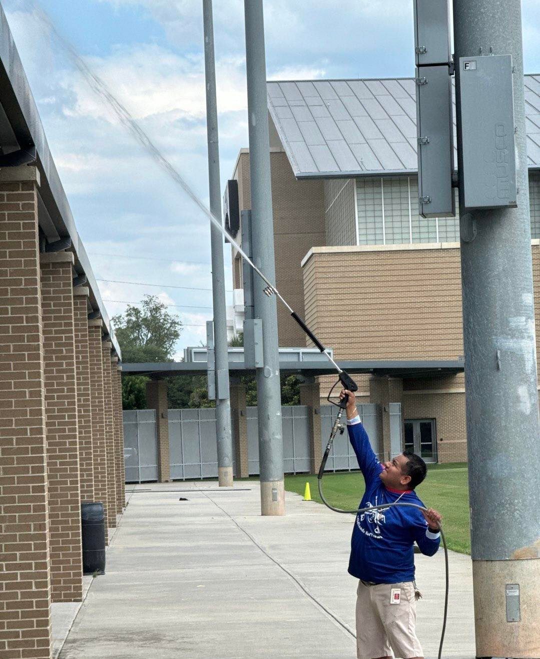 A man is using a high pressure washer to clean a pole.