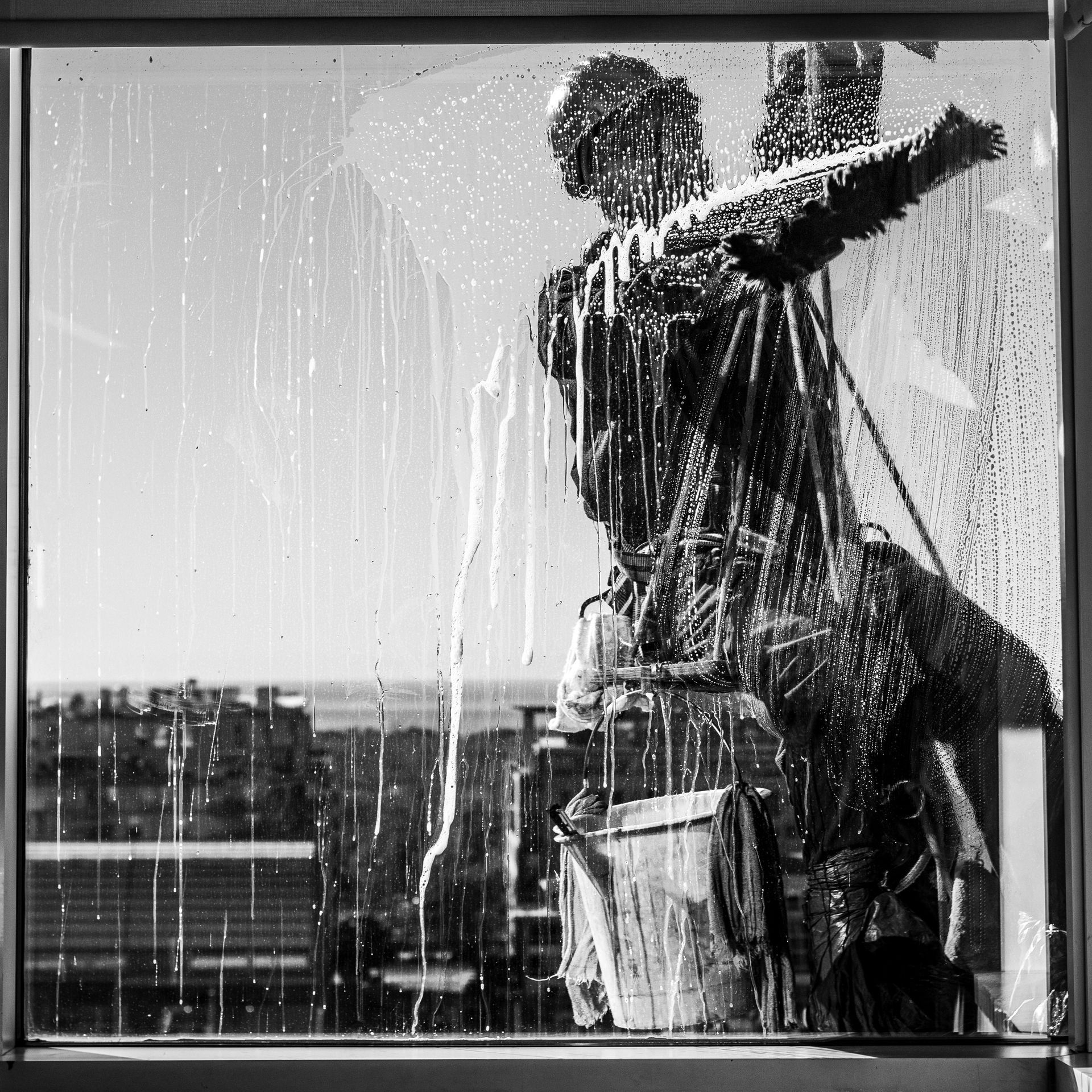 Person washing a window with a squeegee, seen in silhouette behind water streaks.