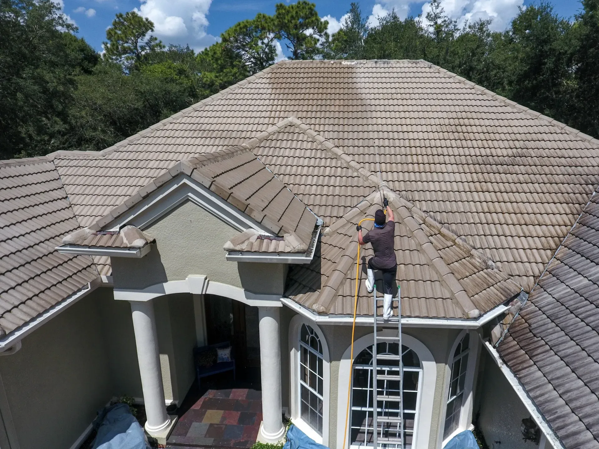 A man is standing on a ladder on the roof of a house.