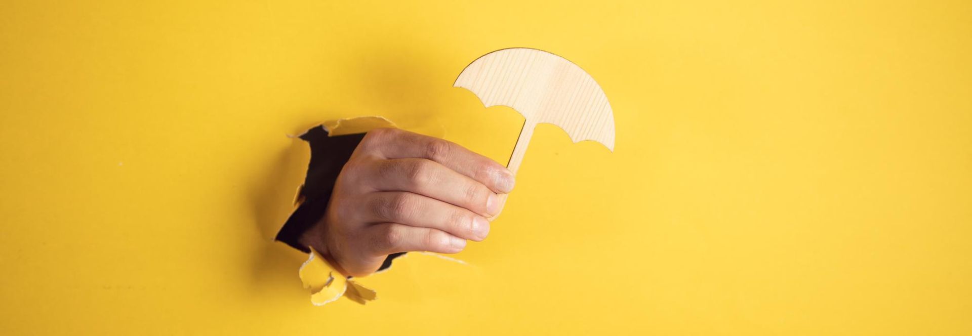 A hand holding a yellow umbrella cutout on a bright yellow background