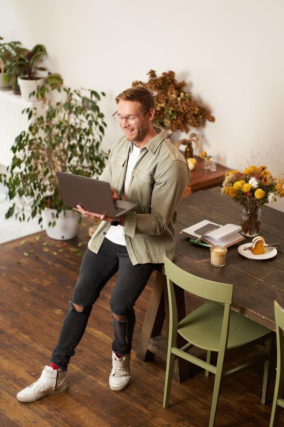 Person using a laptop while standing by a table in a cozy room with plants and flowers