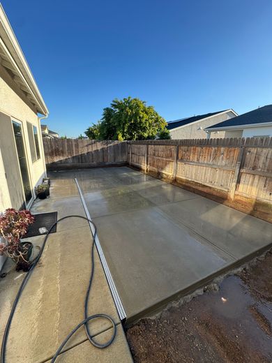 Backyard concrete patio with hose, wet surface, wooden fence, and bright blue sky
