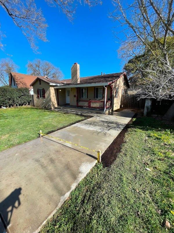 Single-story house with a concrete walkway, front porch, and green lawn under a clear blue sky