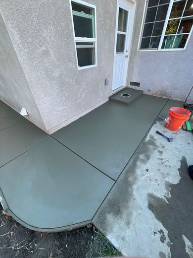 Freshly poured concrete patio beside a stucco house, with windows, a door, and an orange bucket nearby