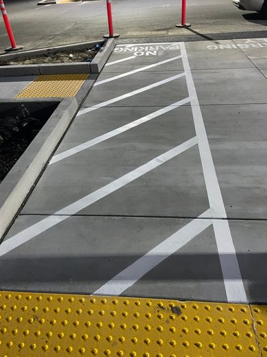 Accessible curb ramp with white diagonal stripes and yellow tactile paving at a street corner