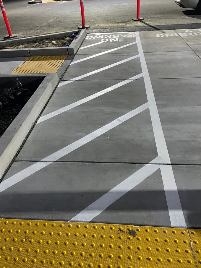 Marked curb ramp with white diagonal stripes and yellow tactile paving at a street corner.