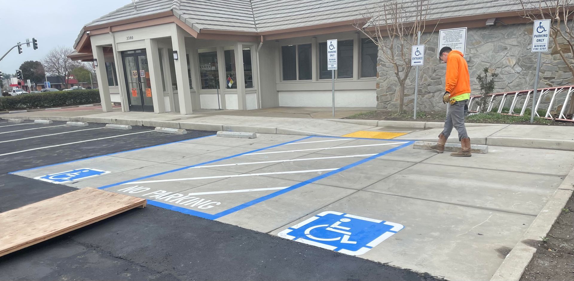 Handicapped parking spaces painted blue in front of a building, with a person in an orange jacket walking nearby