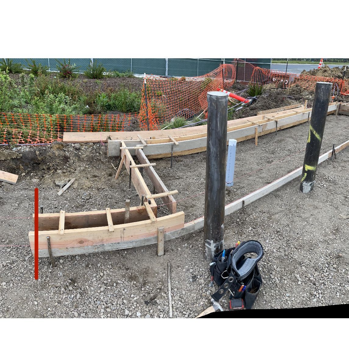 Curved concrete walkway under construction with wooden forms, posts, and gravel on a construction site