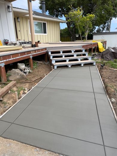Concrete ramp leading to deck stairs beside a yellow house and garden beds