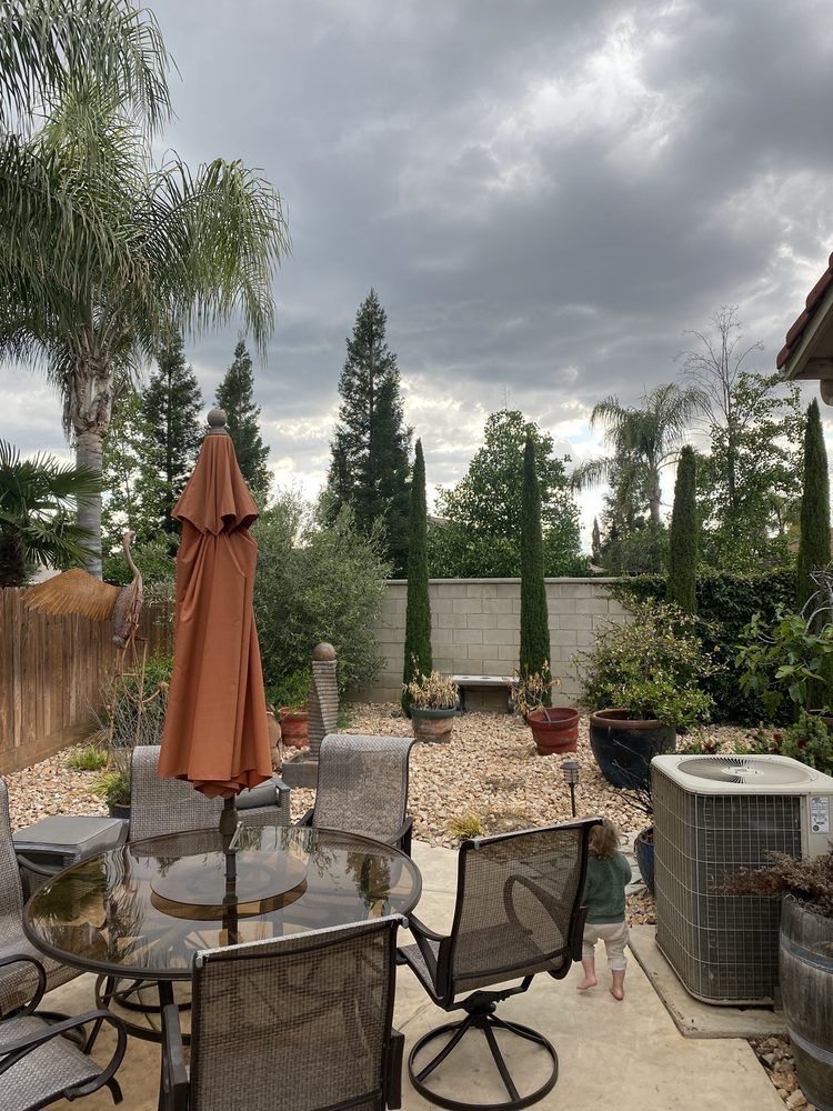Patio with table, umbrella, chairs, potted plants, and a cloudy sky over a gravel garden path.