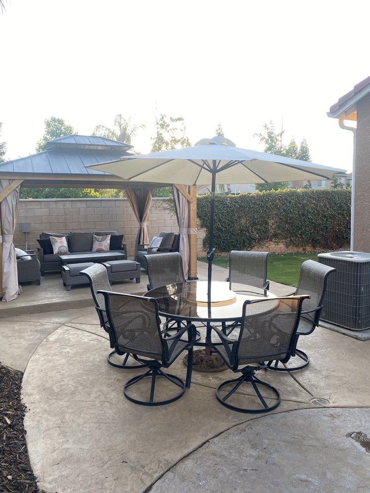 Patio with round glass table, black chairs, large umbrella, and a cushioned gazebo seating area