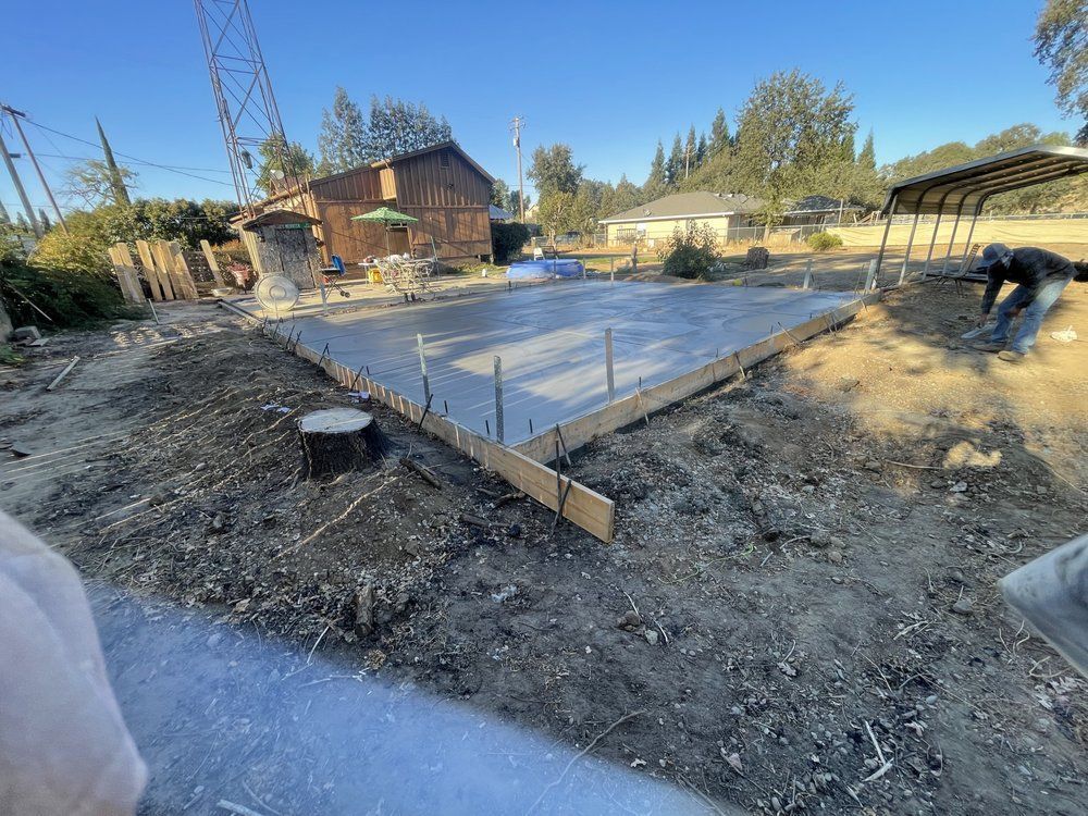 Fresh concrete foundation slab under construction in a backyard, with wooden forms and a worker at right