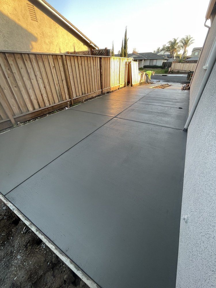 Freshly poured concrete patio beside a wooden fence and house wall at sunset