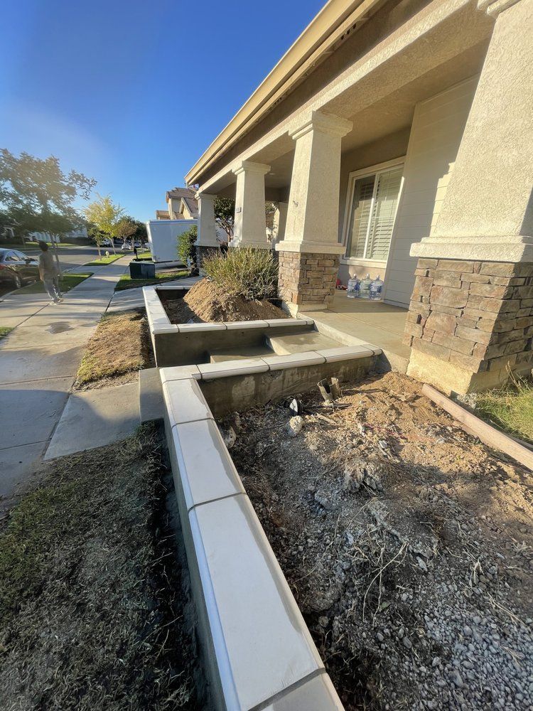 Accessible building entrance with steps, concrete planters, and dry landscaping beside a sidewalk