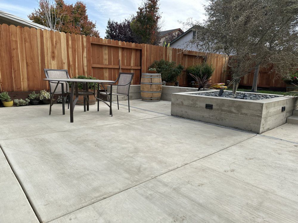 Concrete patio with table and chairs beside raised planter and wooden fence