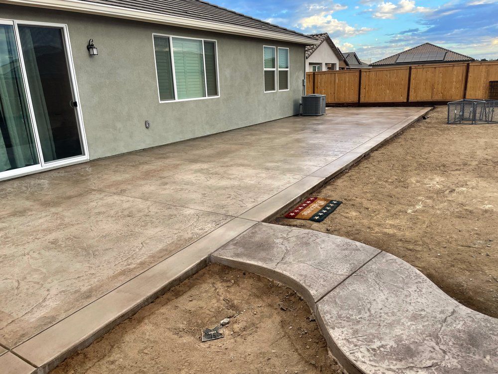 Backyard patio with concrete slab, curved step, and dry dirt yard beside a stucco house