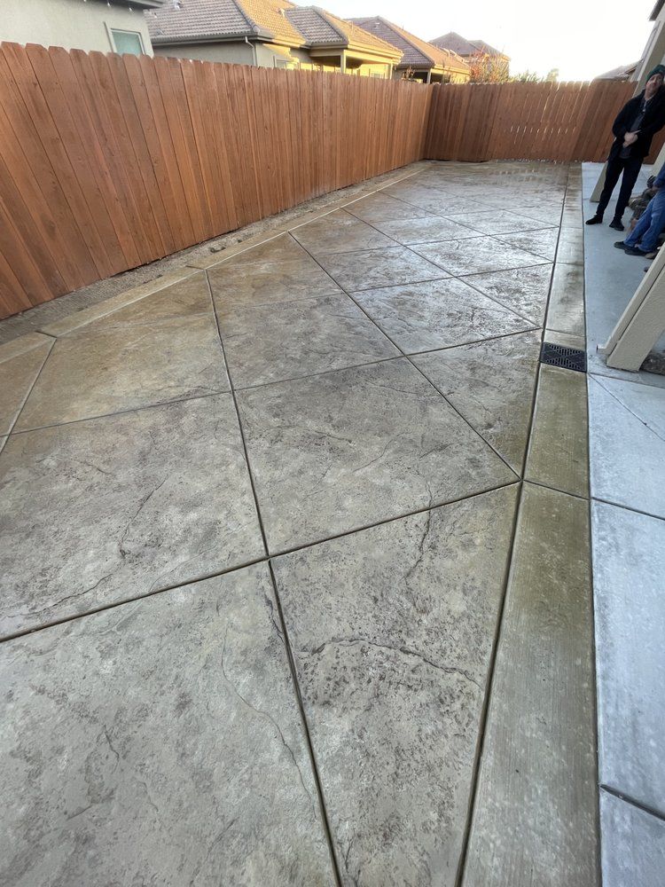 Concrete backyard patio beside a wooden fence, with a person standing at the right edge.