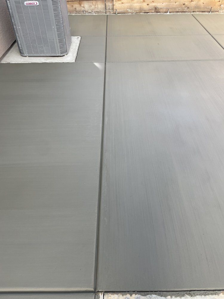 Gray concrete patio with a vertical seam and a planter against a wall in the background