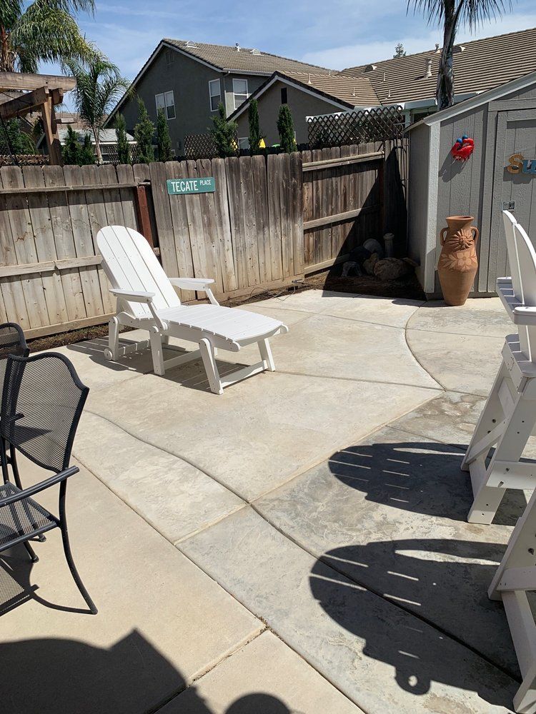 Backyard patio with lounge chairs, wooden fence, and concrete seating area in sunlight