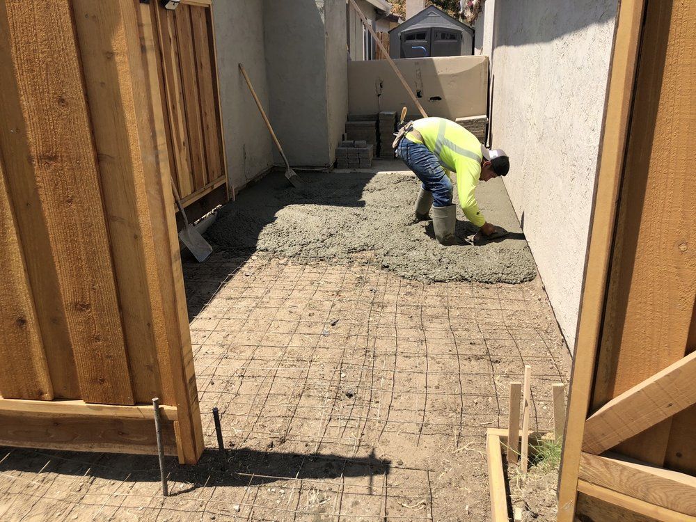 Worker smoothing wet concrete in a narrow construction corridor with wooden framing.