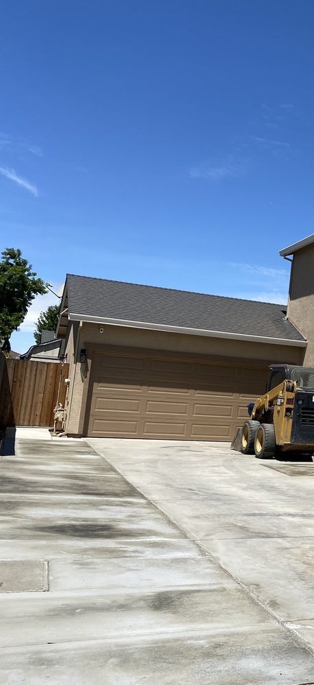 Residential driveway leading to a tan garage under a clear blue sky, with a small construction vehicle on the right